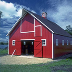 A red barn with doors wide open, against a blue sky with white clouds.